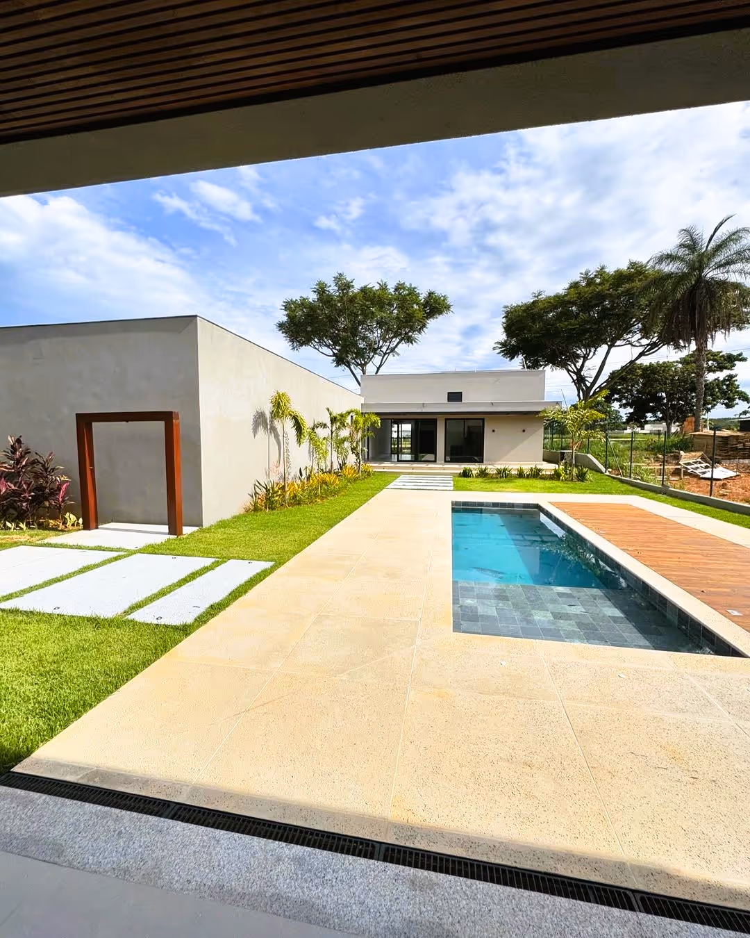 Área externa de casa moderna com jardim, piscina retangular e céu parcialmente nublado.