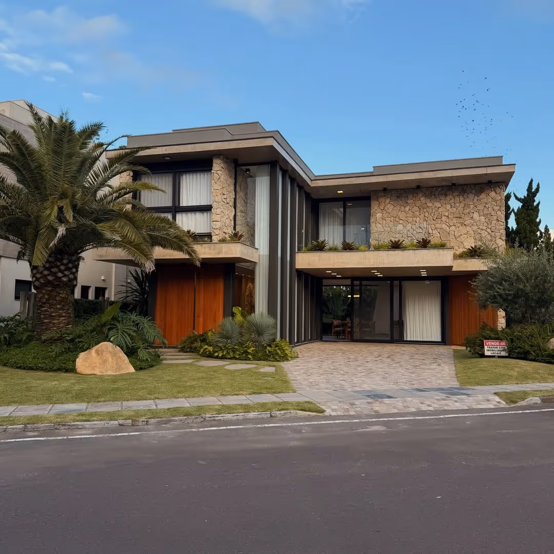 Casa moderna de dois andares com fachada de pedra, grandes janelas, portas de madeira e jardim com palmeira.