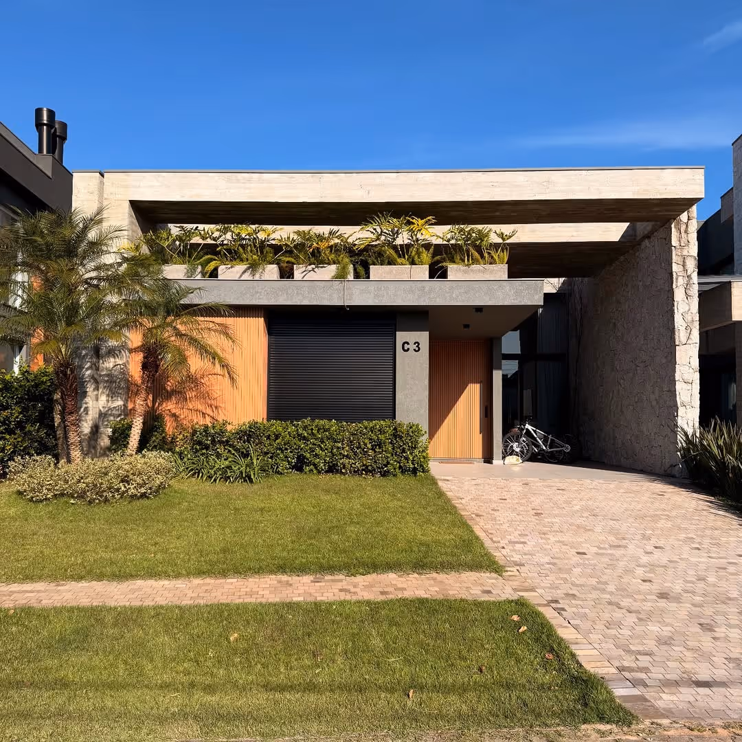 Casa moderna com fachada de concreto, madeira e pedra, jardim gramado na frente e bicicletas na entrada.