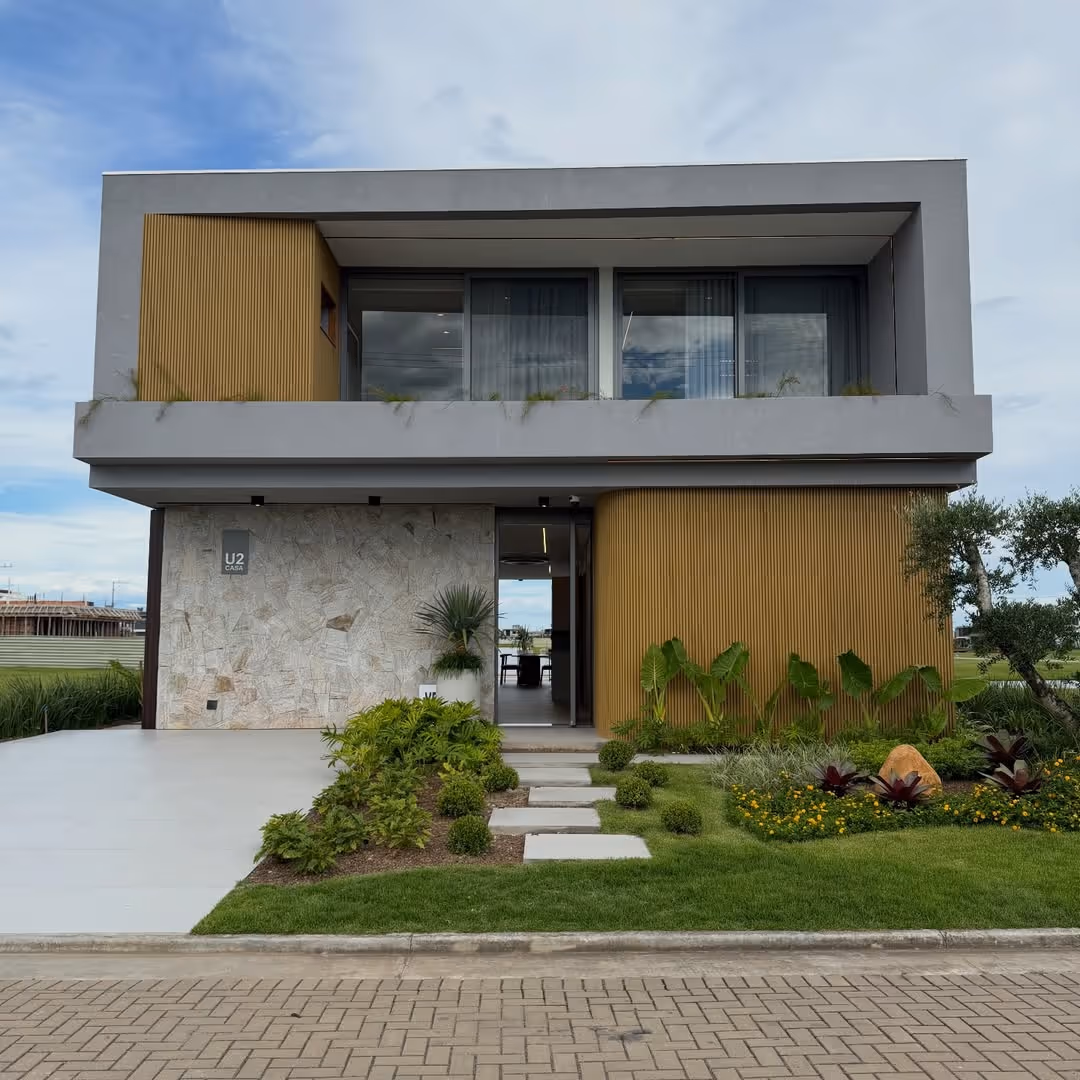 Casa moderna de dois andares com fachada cinza e painéis de madeira, jardim com plantas verdes e caminho de pedras.