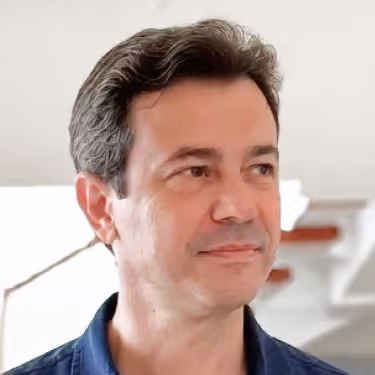 Homem de cabelos grisalhos curtos, olhando para a direita com expressão neutra, vestindo camisa azul.